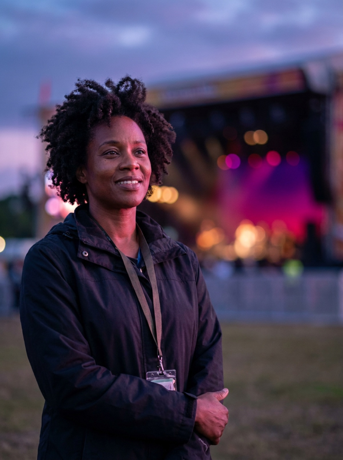 Imani Roswell on the festival grounds at dusk, the stage lit behind her